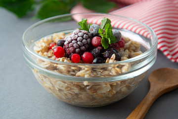 Healthy breakfast in a bowl with oatmeals, frozen berries, fresh strawberries, mint. Oat porridge with fruits.