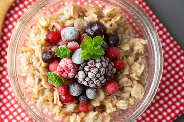 Healthy breakfast in a bowl with oatmeals, frozen berries, fresh strawberries, mint. Oat porridge with fruits. top view.