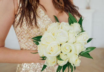 Naklejka premium Crop photo of bride in beautiful golden dress with wedding bouquet of white roses in hands, close up
