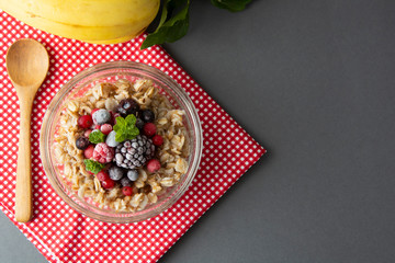 Healthy breakfast in a bowl with oatmeals, frozen berries, fresh strawberries, mint. Oat porridge with fruits. Copy space. Gray background.