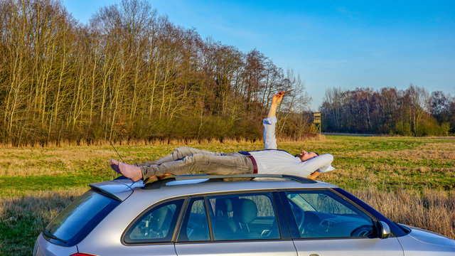 Mann liegt auf einem Autodach und versucht Empfang zu finden, um zu telefonieren, weil er eine Autopanne hat