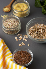 Various uncooked cereals. Different types of groats in bowls on gray background, top view, close up. Healthy nutrition food