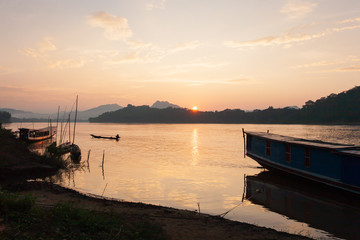 Fisherman steering fishing boat on Mekong River at sunset.