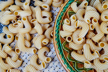 raw whole-grain pasta in a plate on a wicker cloth on the table. top view