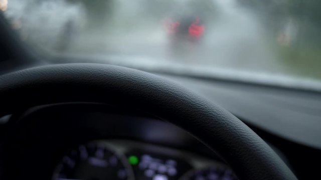Car during heavy rain with emergency gang on. View from windshield to the traffic light under rain. UHD 4K