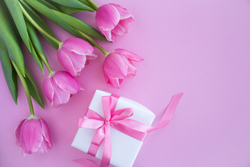 Gift with pink bow and pink tulips on the pink background.Top view.Copy space.