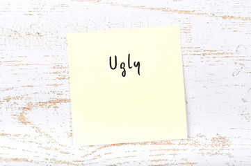 Yellow sticky note with handwritten word ugly