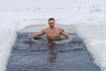 A man bathing in the hole in the winter.