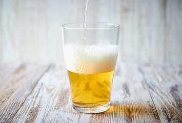 A glass of light beer with foam on a wooden background, close-up. vertical view of the glass.