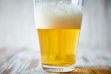A glass of light beer with foam on a wooden background, close-up. vertical view of the glass.