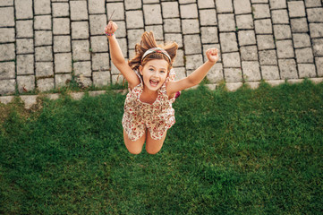 Happy young kid girl playing in summer park, jumping, top view