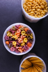 Multicolored pasta with the addition of natural vegetable dye. In a jar on a black concrete table. Top view, copy Space.