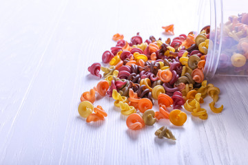 Multicolored pasta with the addition of natural vegetable dye. Scattered from the can on the white table. Top view, copy Space.