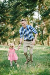 The father runs with a daughter and holds her hand on nature on summer day vacation. Dad and girl walking and playing in the park at the sunset time. Concept of friendly family. Closeup.