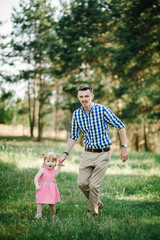 The father runs with a daughter and holds her hand on nature on summer day vacation. Dad and girl walking and playing in the park at the sunset time. Concept of friendly family. Closeup.