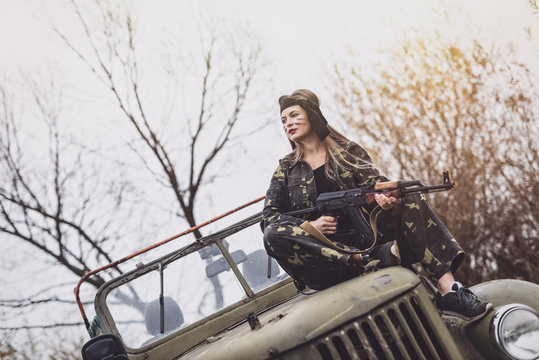 Young woman soldier with rifle posing on military car