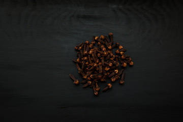 Close-up image of dry cloves on black wood background, view above