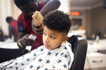 Boy in the african barbershop. Cute mixed boy makes a haircut in the African salon. Hair style. Haircut by machine for children. School boy hair style. 