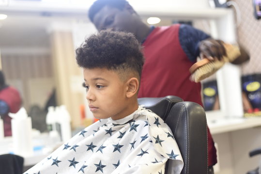 Boy in the african barbershop. Cute mixed boy makes a haircut in the African salon. Hair style. Haircut by machine for children. School boy hair style. 