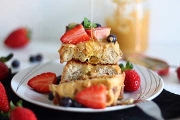 Pouring syrup over french toasts with peanut butter, strawberries and blueberries for breakfast.