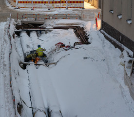Two workers welding on a big pipe among the snow in a urban construction site, Helsinki Finland