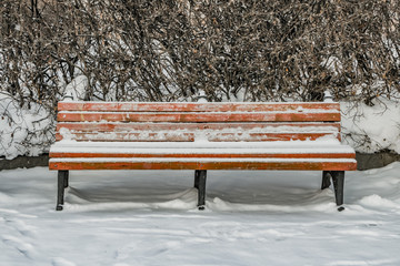 A wooden painted brown color beautiful bench with black wrought-iron legs stands with white snow in a park in winter