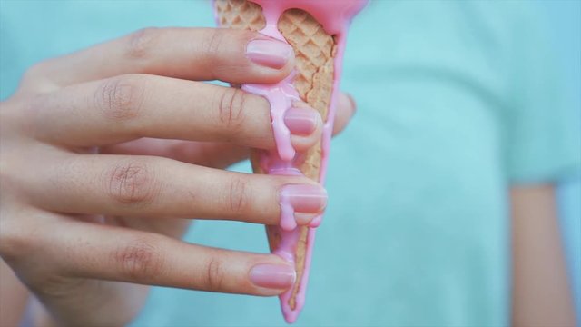 young afro girl eating pink melting ice cream at blue wall background