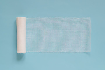 Unwound roll of white sterile medical bandage for dressing wounds on a blue background, copy space