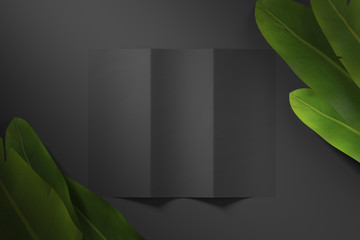 Blank black paper sheet on matte background with green tropical leaves. Top view. Mock up. 3d rendering