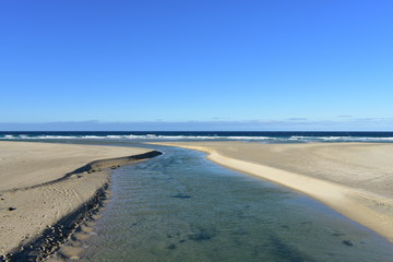 Beach with golden sand, river and blue sea with waves and white foam. Clear sky, sunny day. Galicia, Spain.