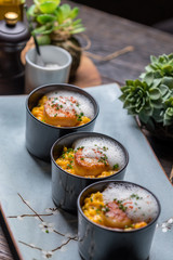 Orange pumpkin risotto with scallop and foamy sauce in black bowl on rustic wooden table