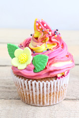 Colorful cupcake with sugar flowers on a wooden table.  Close-up