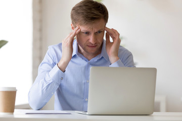 Tired businessman sitting at desk suffering from headache