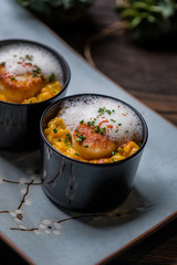 Orange pumpkin risotto with scallop and foamy sauce in black bowl on rustic wooden table