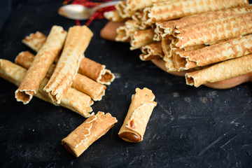 Wafer rolls, tasty and fragrant, with boiled condensed milk on a black table