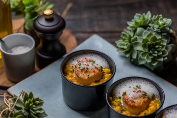 Orange pumpkin risotto with scallop and foamy sauce in black bowl on rustic wooden table