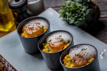 Orange pumpkin risotto with scallop and foamy sauce in black bowl on rustic wooden table