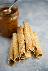 Waffle rolls, tasty and fragrant, with boiled condensed milk on a concrete background