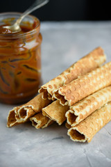 Waffle rolls, tasty and fragrant, with boiled condensed milk on a concrete background