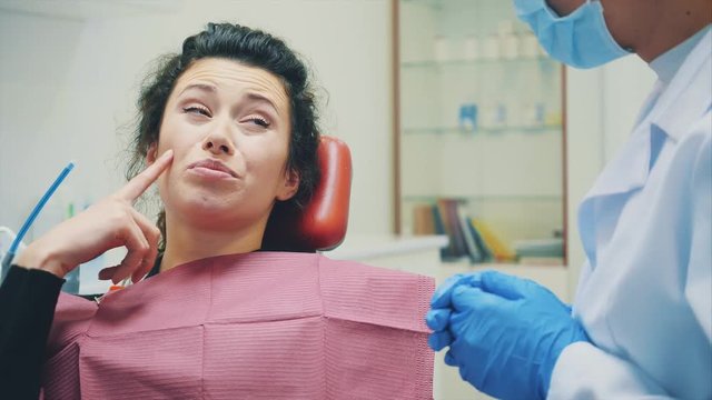 Unhappy woman from pain. Having a toothache and visiting a dentist. Shows the place of pain.