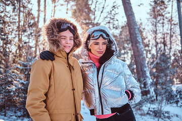 Happy family. Smiling mom and her son dressed in stylish warm clothes standing in hug in the snowy forest during sunrise