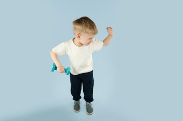 sporty little boy with dumbbells shows his muscles on an isolated blue background. The concept of a healthy lifestyle