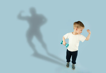 sporty little boy with dumbbells shows his muscles on an isolated blue background. The concept of a healthy lifestyle