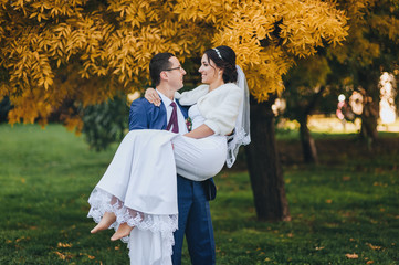Naklejka premium Happy young newly married wedding couple on walk in golden yellow fall autumn park around trees. Groom circling bride in beautiful white dress. Relationship love concept. Man woman on nature outdoors