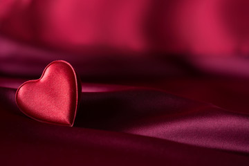 Single isolated red heart lying on its side on purple satin