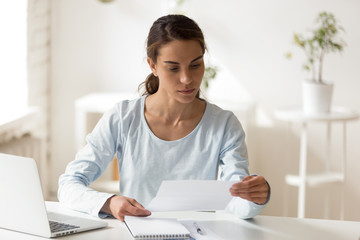 Serious woman sitting at desk reading letter