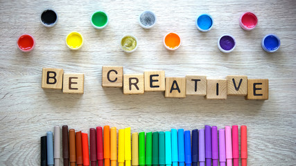 Be creative phrase made of cubes, colorful felt-tip pens and paints lying table
