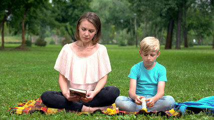 Son bored while mother reading book about child education, tips for parents