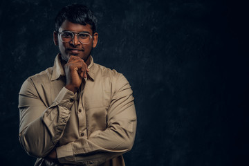 Confident Indian man in eyewear and shirt looking at a camera with a thoughtful look in dark studio