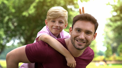 Son and father posing on camera, enjoying piggyback ride, fooling around, fun